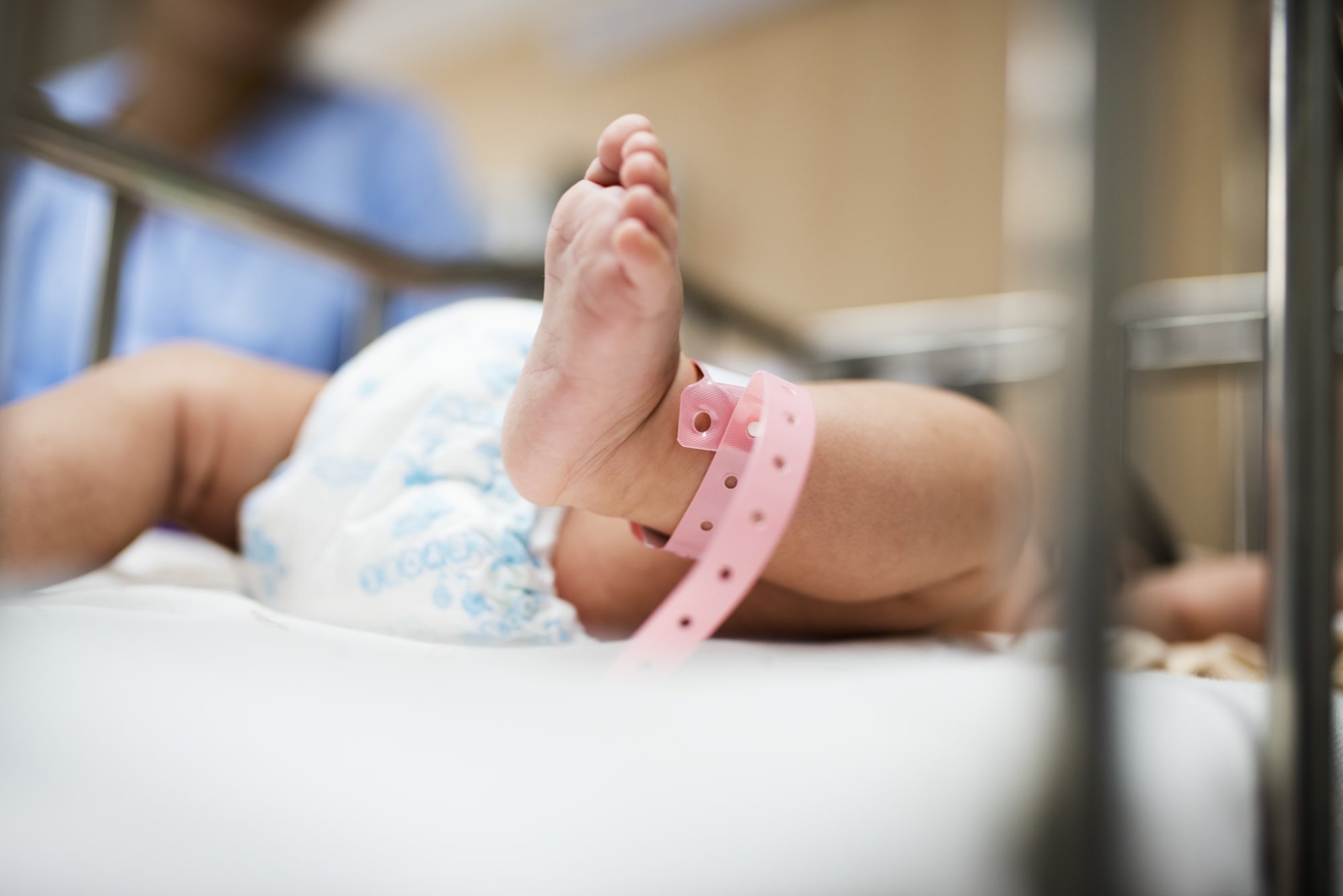 A baby lying in a hospital bed, wearing a diaper, with a peaceful expression and surrounded by medical equipment.